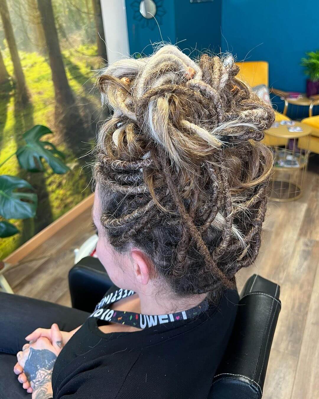 Voluminous bun made of blond dreadlocks atop the head, intricately woven with threads.