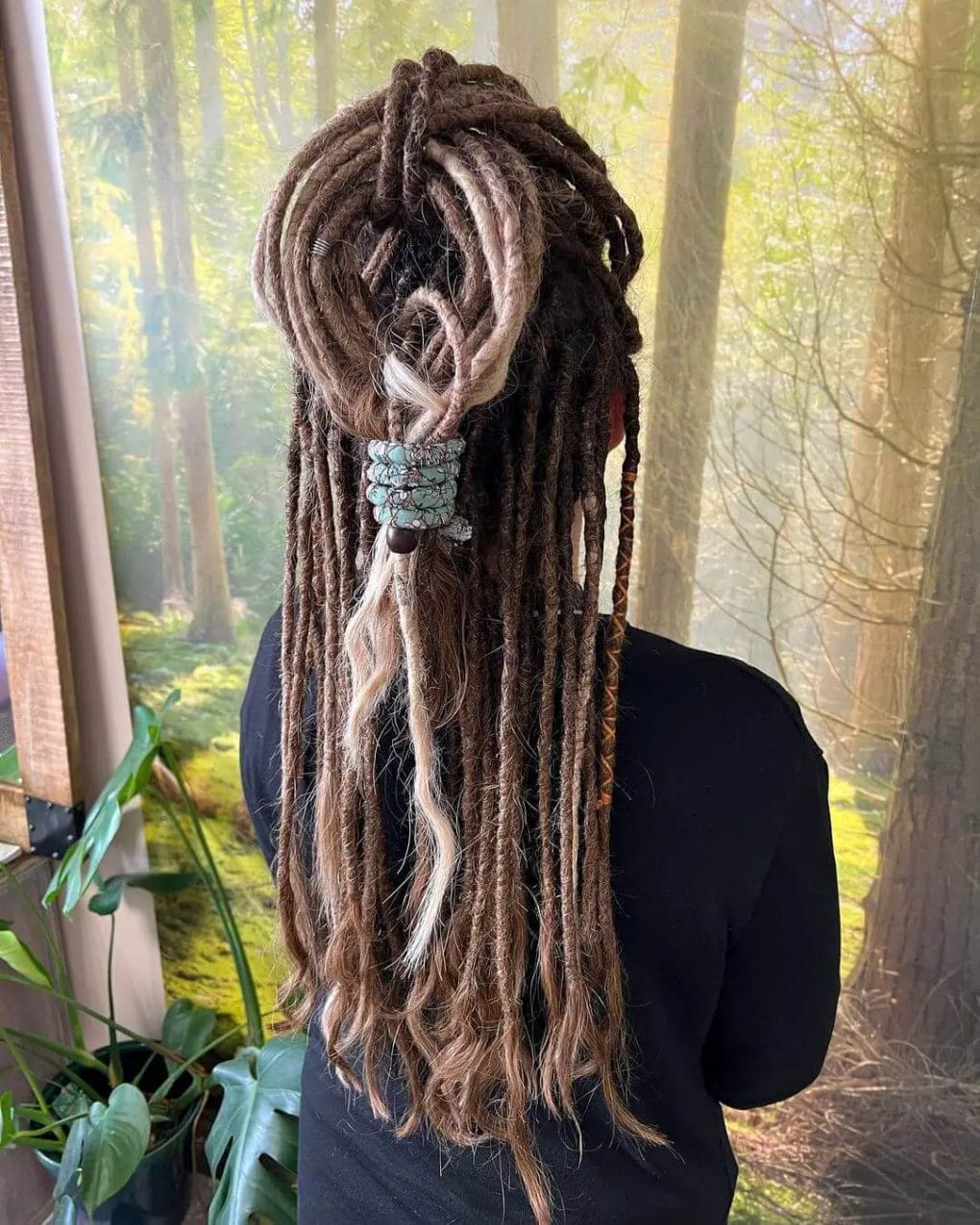 Brunette dreadlocks with blonde highlights, adorned with threads and beads, and fashioned into a loose braid down the back.