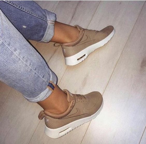 Tan sneakers with a smooth leather upper, cushioned ankles, and retro air cushioning, styled with light blue jeans on a wooden floor.