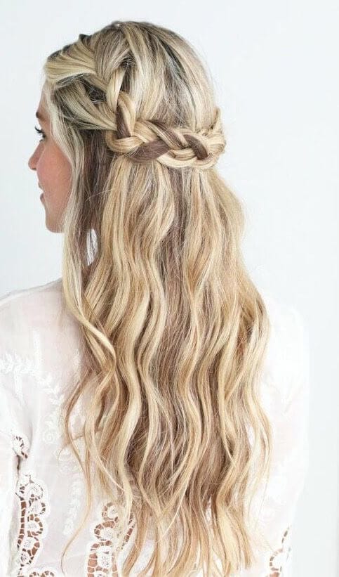 Loose, wavy hair styled in a half up, half down bun, featuring a braided crown and natural blonde highlights, perfect for casual or formal occasions.