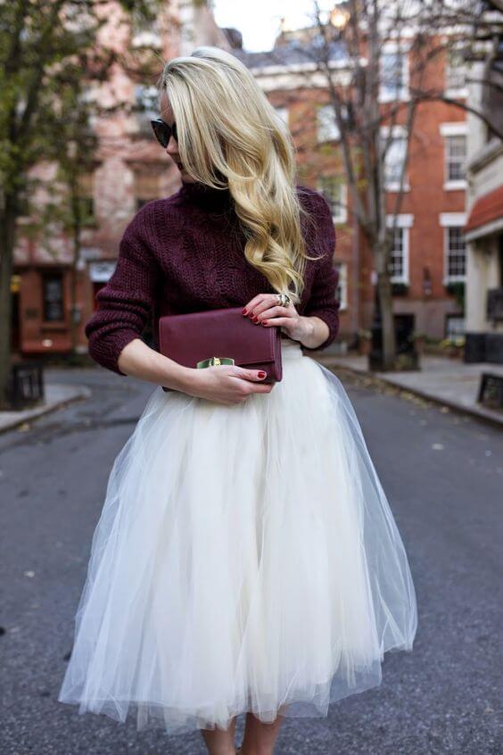 Long blonde hair styled in soft waves complements a fitted maroon sweater and airy white tulle skirt, perfect for chic winter outfits.