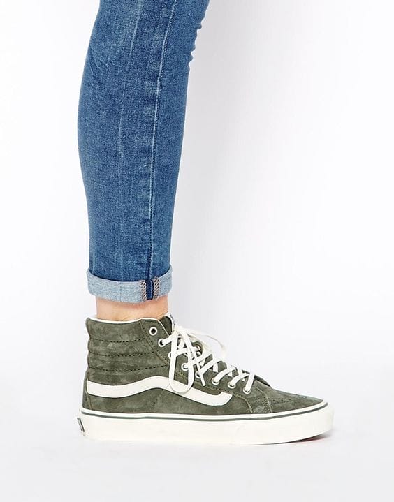 High-top olive green suede sneakers with a white stripe, paired with rolled ankle-length denim jeans, creating a stylish, casual look.