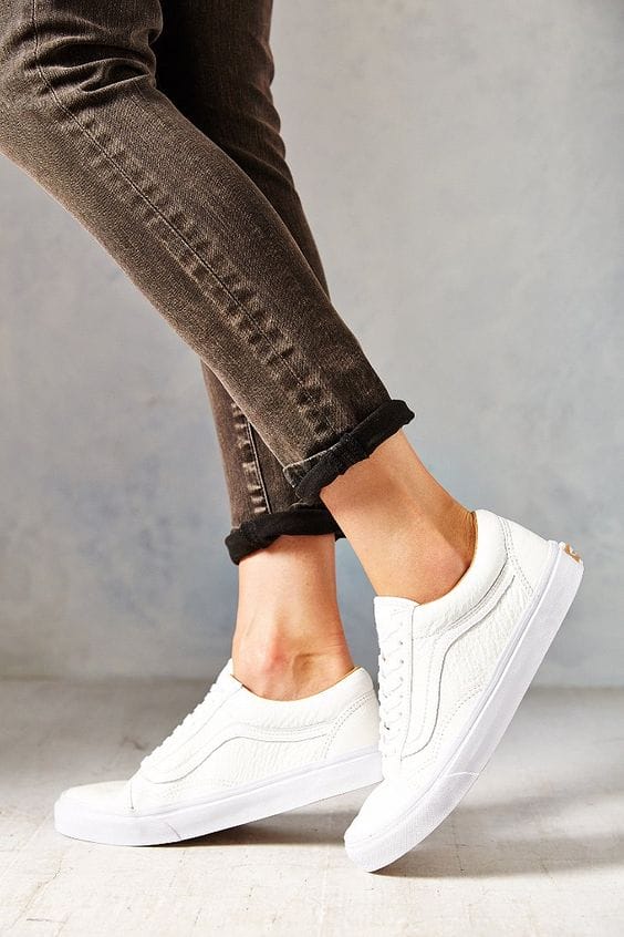 White sneakers with a sleek design and textured finish, paired with dark, rolled cuff jeans for a trendy everyday look.