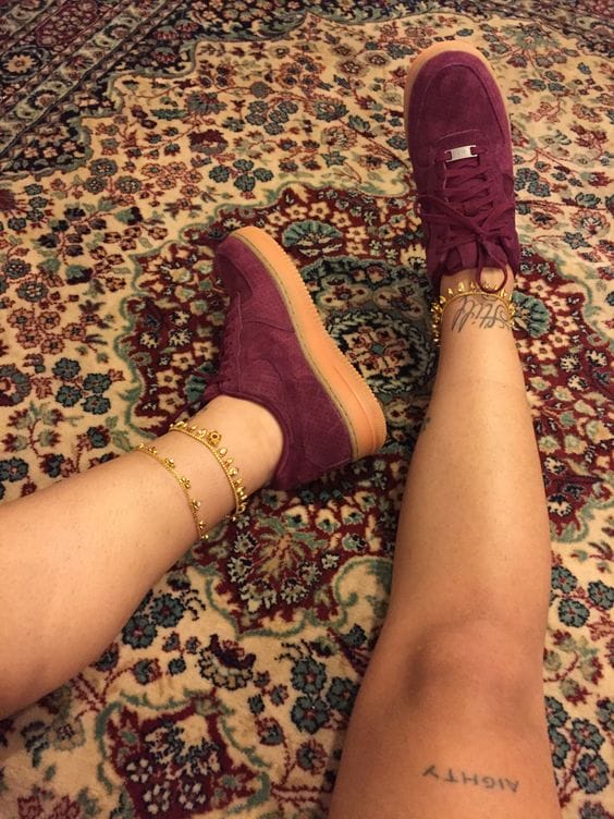 High-top sneakers in deep plum suede, featuring rubber soles for traction and gold ankle cuffs. Set against a patterned rug backdrop.