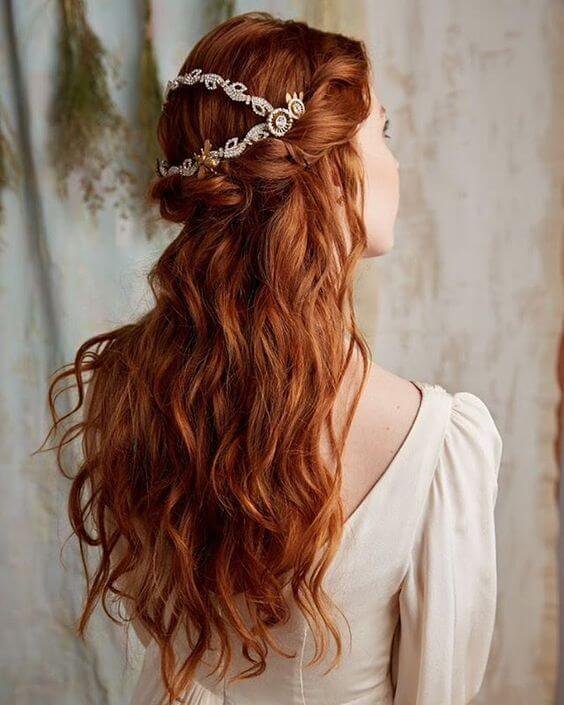 Wavy auburn hair styled in a half up half down bun with soft waves. A delicate stone-adorned accessory adds elegance, perfect for formal occasions.