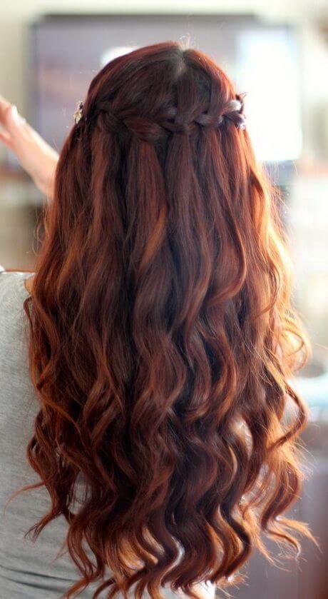 Wavy hair styled in a half-up, half-down bun with delicate braids at the crown, offering a voluminous and elegant look.