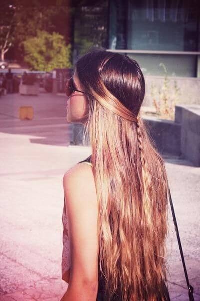 Long hair styled in a half up, half down bun with a small braid at the crown. Urban backdrop with greenery, creating a casual summer vibe.