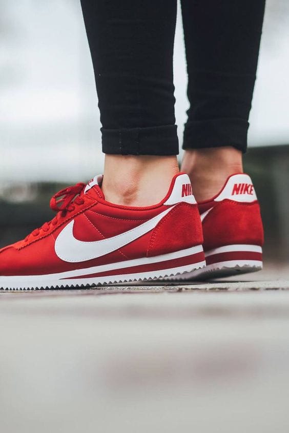 Vibrant red low-top sneakers with a white swoosh, paired with black fitted pants, showcasing style and comfort for women.