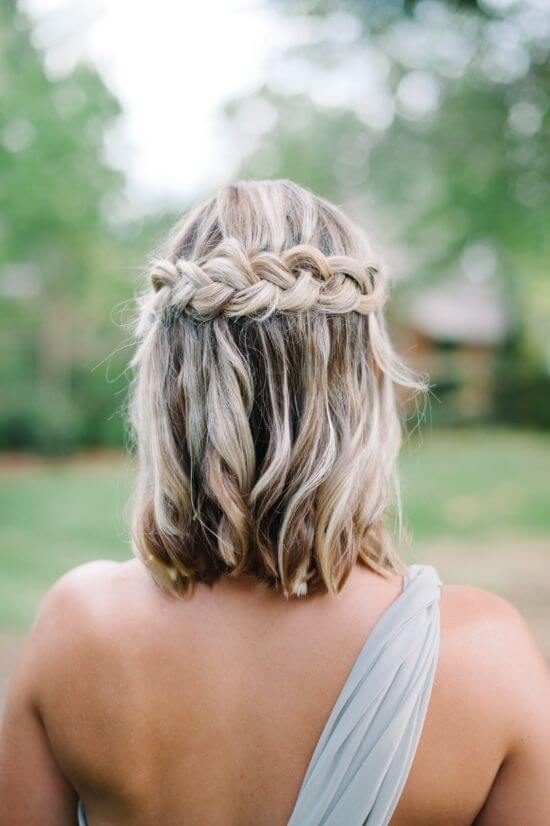 Braided crown hairstyle with medium-length wavy blonde hair, loose waves cascading down, perfect for warm outdoor events and elegant dresses.