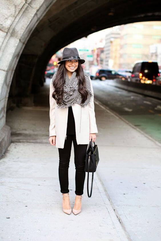 Chic winter outfit featuring a cream oversized coat, black top, skinny pants, checkered scarf, and a felt hat, perfect for casual outings.