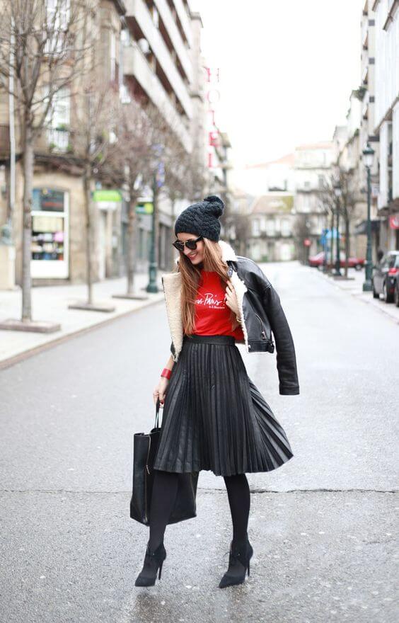 Chic winter outfit featuring a ribbed black pleated midi skirt, vibrant red graphic tee, and a shearling-lined leather jacket.