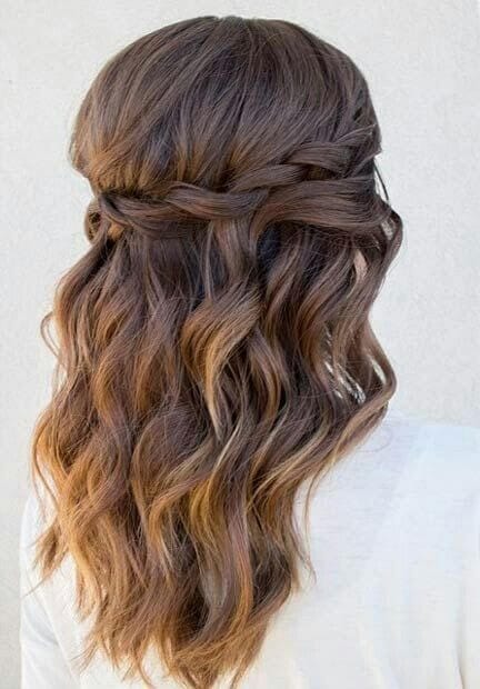 Wavy half up, half down bun features cascading waves, twisted braid, and a rich dark brown to caramel color gradient, perfect for formal occasions.