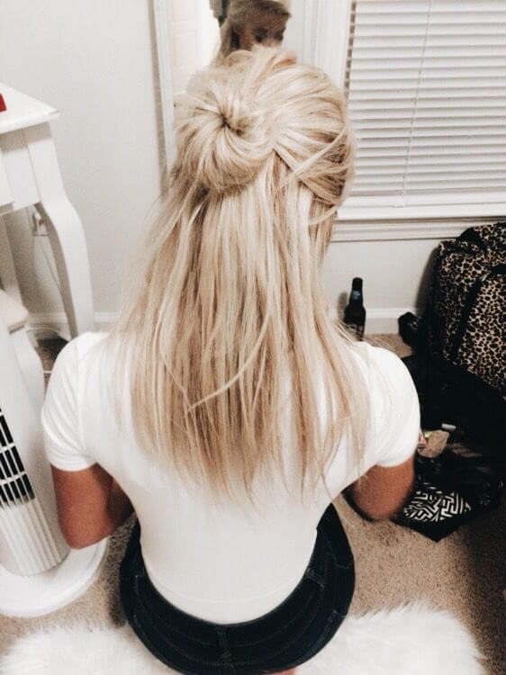 Soft, wavy blonde hair styled in a half up half down bun, with a twisted knot at the crown, against a neutral backdrop.