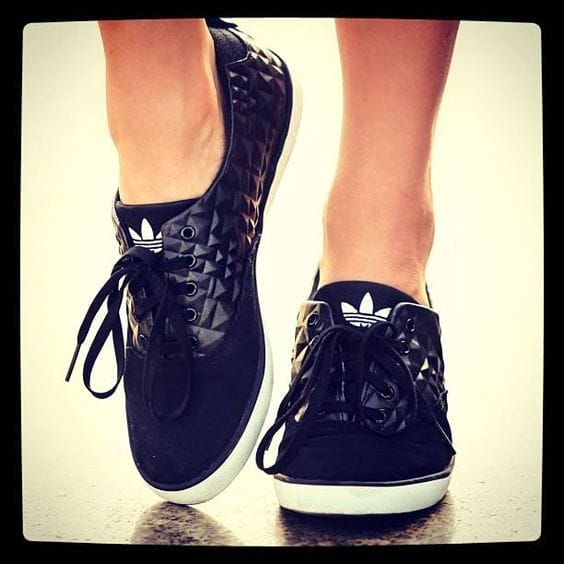 Stylish women's sneakers with a black textured pattern and glossy finish on the left, solid black on the right, featuring classic lace closures.