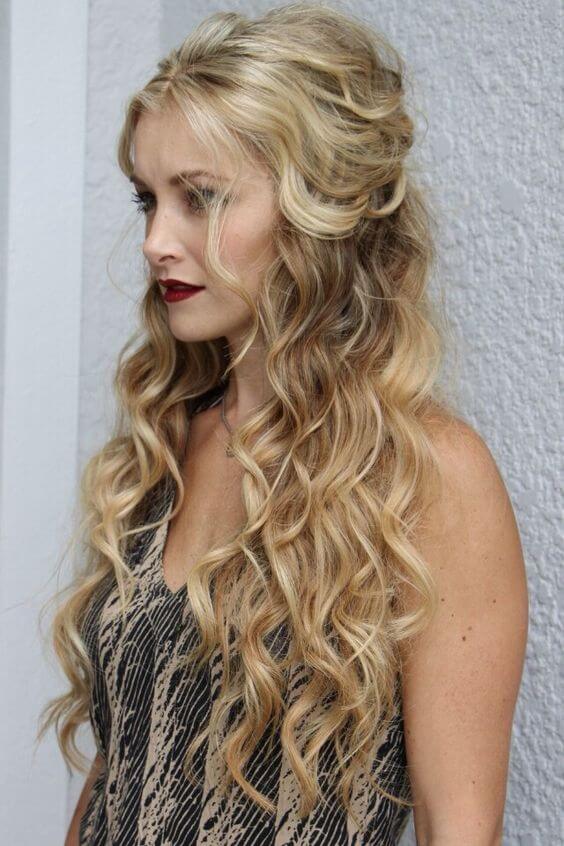 Long wavy hair styled in a half up half down bun, featuring voluminous curls and warm blonde hues, perfect for casual chic looks.