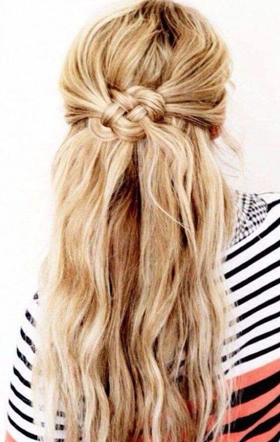 Half-up, half-down bun with a braided knot at the crown, featuring loose, wavy blonde strands cascading to mid-back.