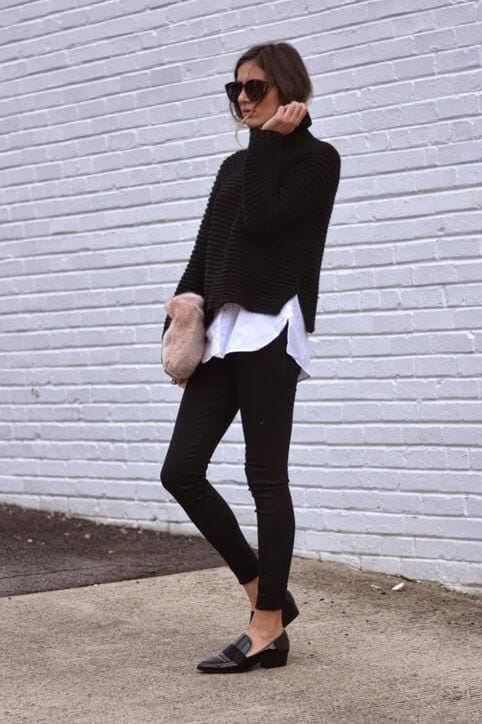 Relaxed black knitted turtleneck sweater layered over a white shirt, paired with fitted black trousers and loafers. Stylish winter office wear.