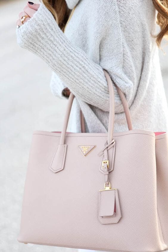 Sophisticated handbag in soft beige leather, structured design with sharp corners, dual top handles, and gold-tone clasp tag.