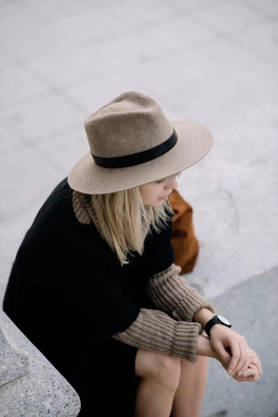 A woman wears a structured beige felt hat with a wide brim and black ribbon, paired with a dark oversized sweater, exuding casual elegance.