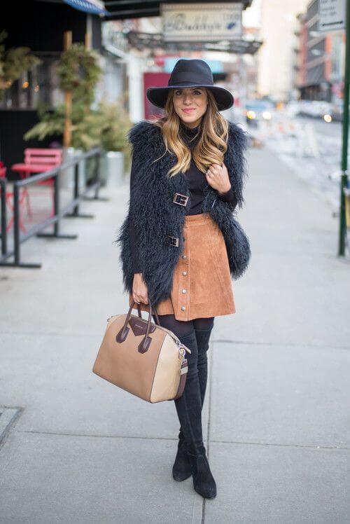 Stylish women's winter hat paired with a chic urban outfit, featuring a black faux fur vest and knee-high black suede boots.