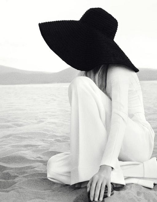 Wide-brimmed straw hat offers ample shade, paired with a light outfit for a relaxed beach vibe, emphasizing minimalist style.