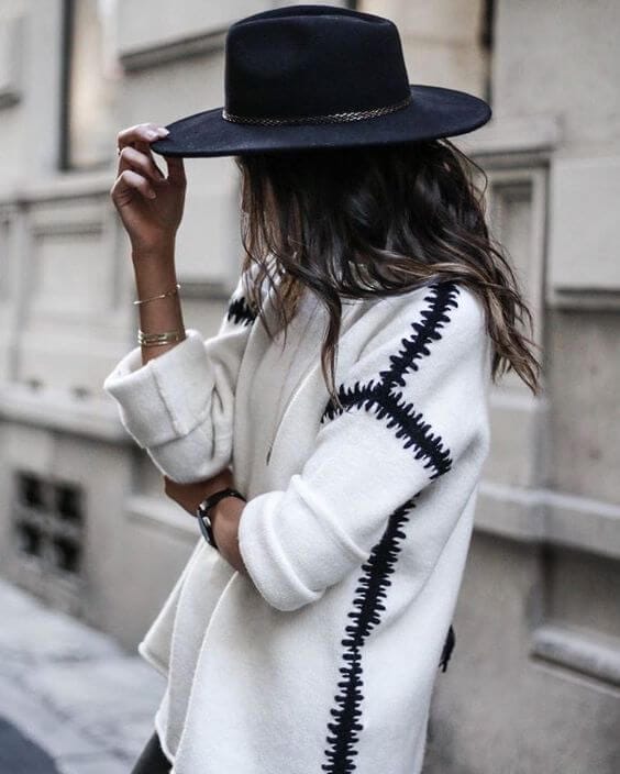 A woman models a black wide-brimmed hat with a stylish white oversized cardigan, perfect for winter fashion.