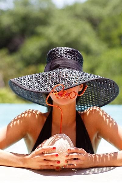 Stylish wide-brimmed women's straw hat made of black textured material, elegantly shielding the face by the water, perfect for beach outings.