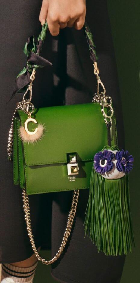 Stylish green handbag with a shiny patent finish, featuring a structured shape, fluffy charm, and floral tassel. Versatile dual strap design.