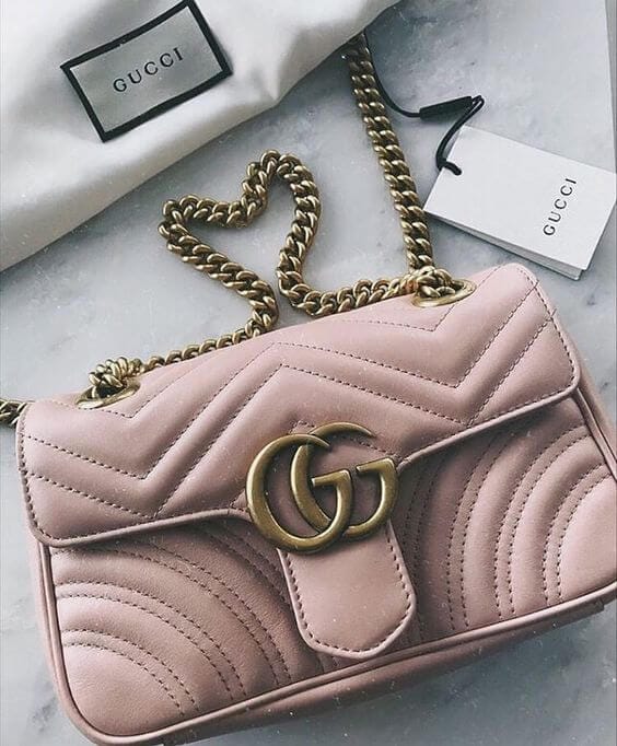 Handbag with a quilted pink design, gold GG logo, gold chain strap, and fabric-lined interior, displayed on a marble surface.