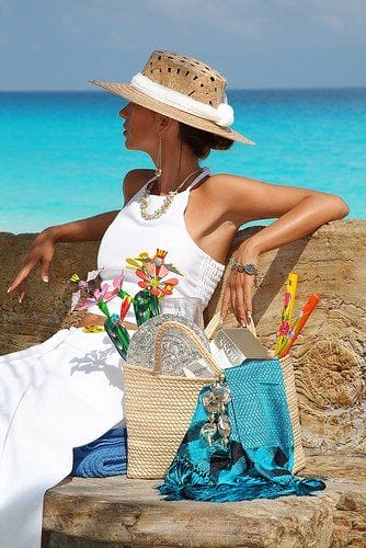 Wide-brimmed straw sun hat with a decorative band, paired with a flowing white dress, set against turquoise waters and a clear sky.