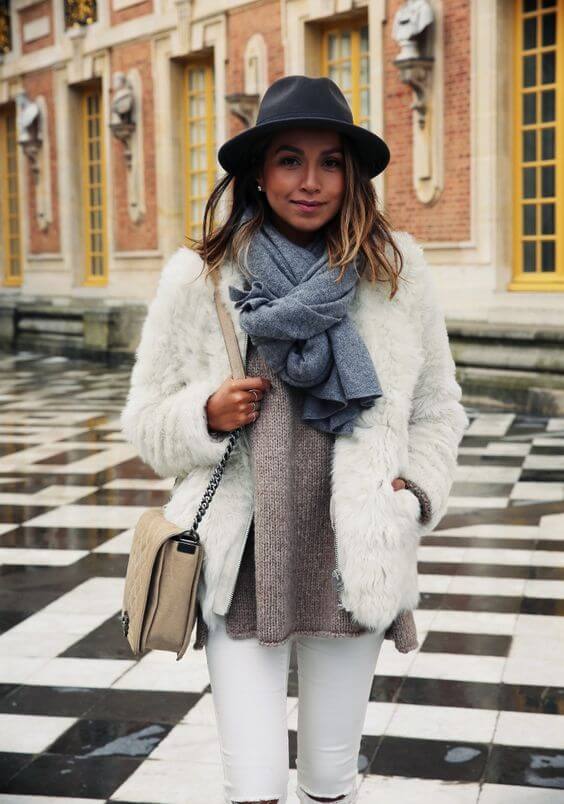 Cozy winter outfit with a wide-brimmed black hat, paired with a stylish white faux fur coat and chunky knit sweater.