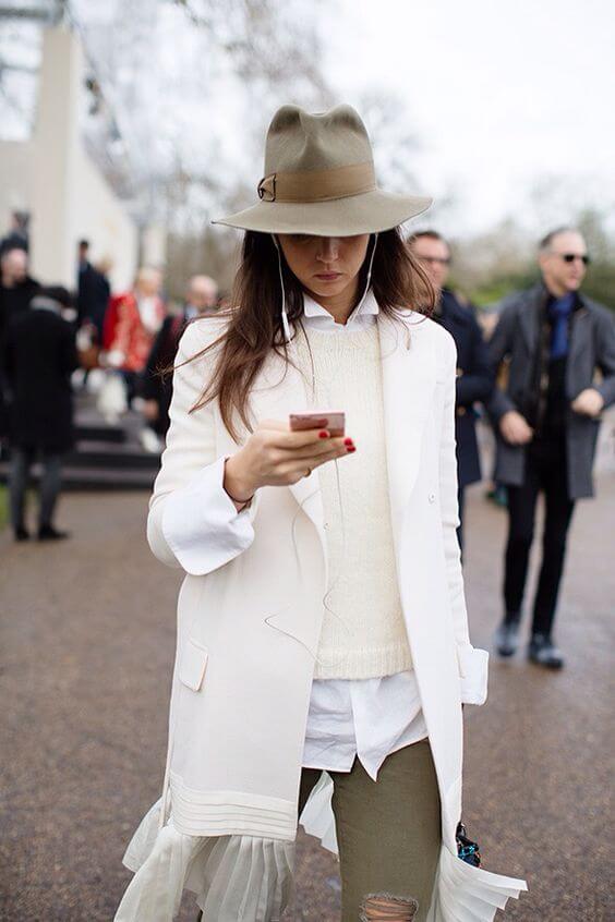 A woman wears a stylish light beige wide-brimmed winter hat, paired with a tailored coat and layered clothing, perfect for cold weather.