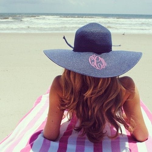 Wide-brimmed navy beach hat with monogram detail, perfect for sun protection, set against sandy beach and ocean waves.