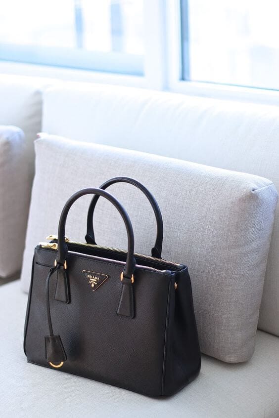 A structured black handbag with top handles and zip closure, crafted from durable leather, positioned on a light sofa.