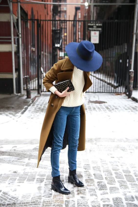 A stylish wide-brimmed navy hat complements a cozy cream sweater and wool coat, perfect for winter fashion in an urban setting.