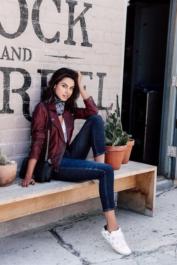 Soft waves frame the face, paired with a maroon leather jacket, white top, and skinny jeans. A chic fall outfit against a brick wall.