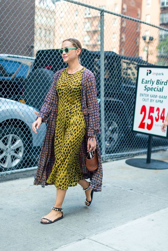 Sleek, pulled-back hairstyle complements a flowy, layered yellow leopard print dress, styled with chunky sandals in an urban setting.