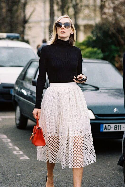 Chic outfit featuring a black ribbed turtleneck and a white midi skirt with eyelet pattern, accessorized with oversized sunglasses and a red handbag.