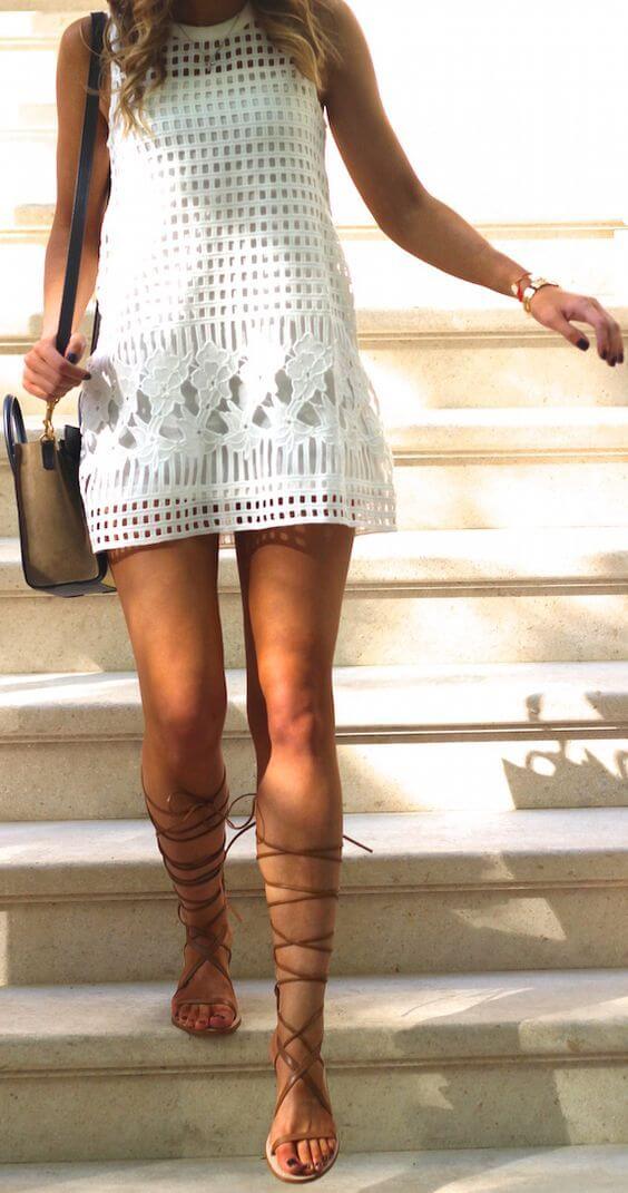 White dress with a grid pattern and floral embroidery, knee-length, paired with beige strappy sandals and a small black handbag.