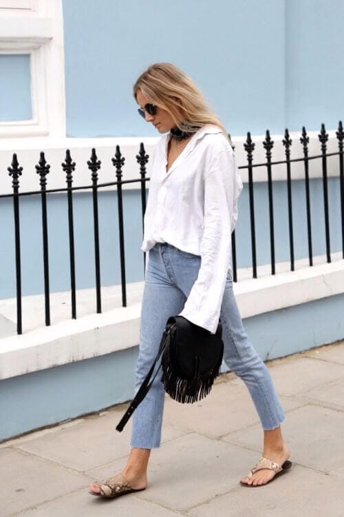 Wavy, shoulder-length hair complements a model's relaxed outfit: a white button-down shirt and light blue high-waisted jeans, paired with stylish sandals.
