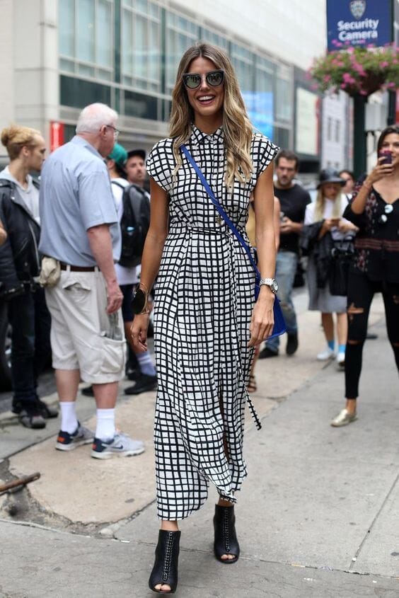Long checkered dress with a high slit, paired with black heeled boots, sunglasses, and a crossbody bag in an urban setting. Stylish and functional.