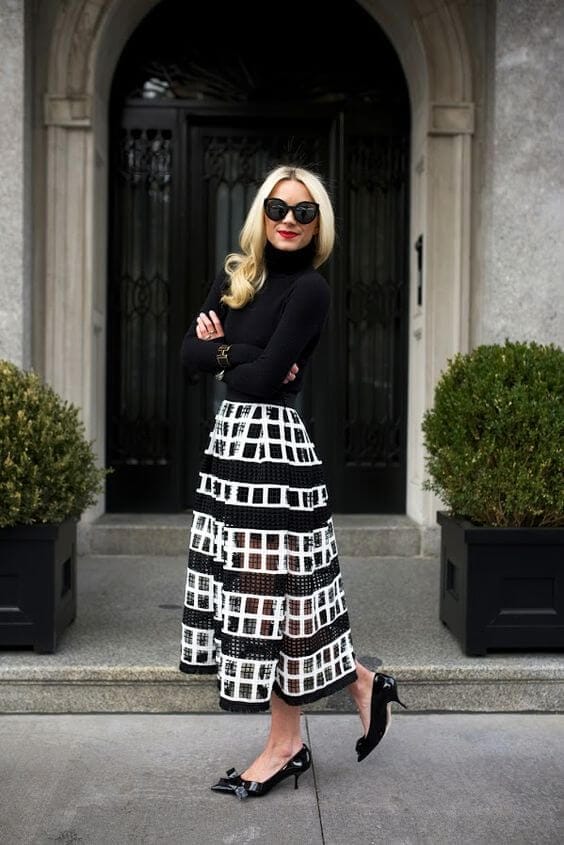 Long, sleek blonde hair with soft waves complements an elegant black turtleneck and a black and white grid-patterned skirt, creating a chic urban look.