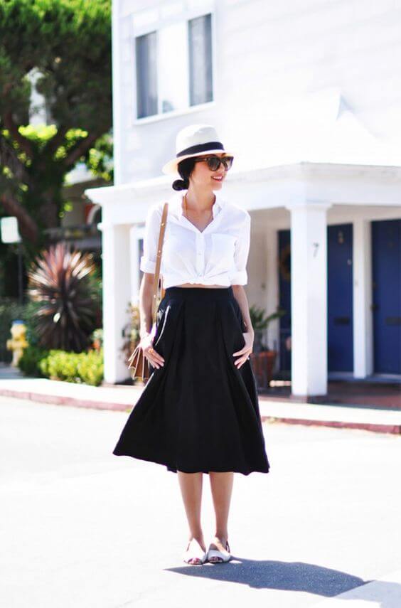 Crisp white shirt with rolled three-quarter sleeves paired with a flowing black midi skirt, accessorized with a wide-brimmed hat and oversized sunglasses.