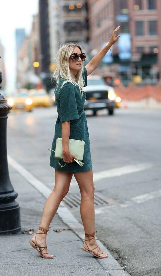 Casual urban outfit featuring a forest green knee-length dress, tan sandals, oversized sunglasses, and a light green clutch.