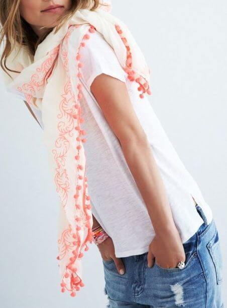 Lightweight floral scarf with pom-pom edges, 70x26 inches, styled with a white t-shirt and denim shorts for a chic summer look.