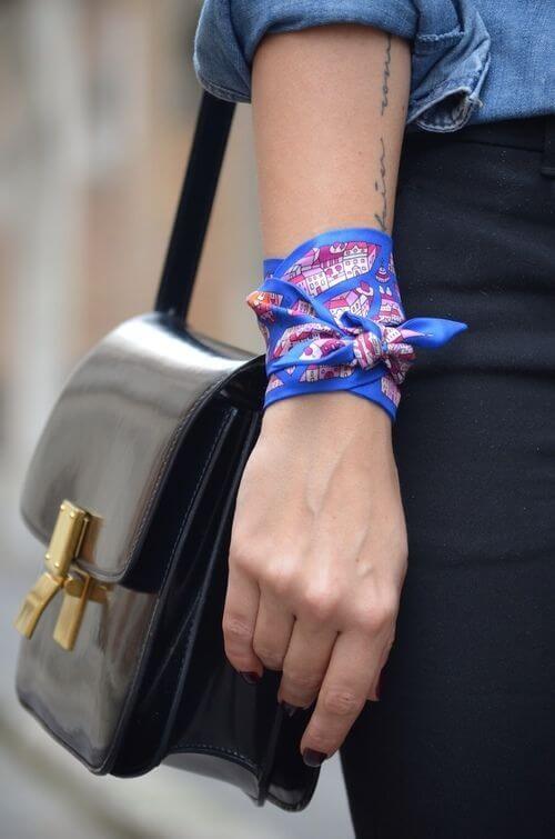 Silk handkerchief tied in a bow on a wrist, featuring colorful prints. Worn with a denim shirt and a black leather handbag.