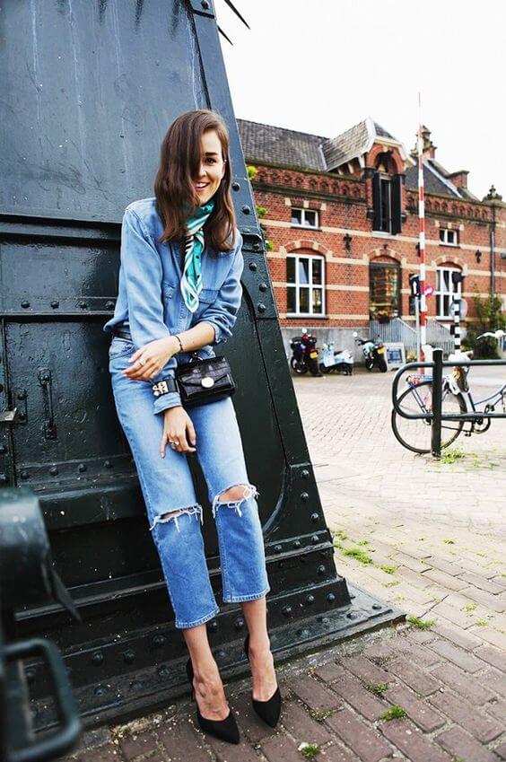 Stylish summer outfit featuring a light blue denim jacket, distressed jeans, and a silk green and white scarf against a rustic backdrop.