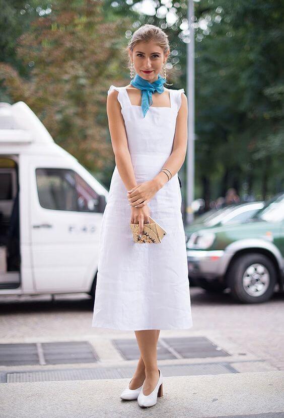 Turquoise silk scarf tied at the neck complements a knee-length summer dress with square cutouts and shoulder straps, perfect for warm weather.
