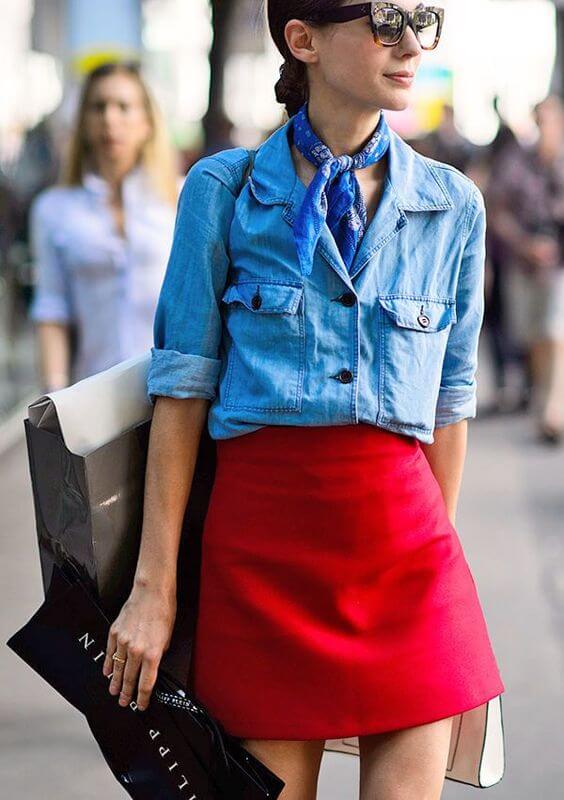 Denim jacket with cropped sleeves and front pockets, paired with a high-waisted red mini skirt, accented by a blue silk scarf and oversized sunglasses.