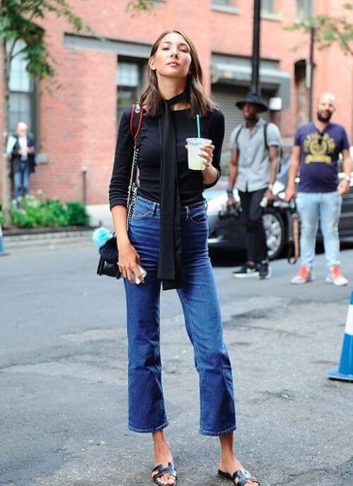 Model wears a fitted black long-sleeve top and high-waisted cropped blue jeans, accessorized with a silk scarf, exuding chic summer style.